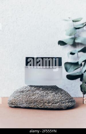 Pot de produit naturel de soin de la peau sur podium en pierre naturelle avec branche d'eucalyptus, vue avant. Fond gris en pierre. Maquette. Banque D'Images