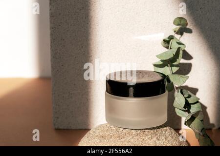 Pot de crème, produit de soin naturel de la peau sur podium de pierre naturelle avec branche d'eucalyptus au soleil. Arrière-plan beige. Maquette. Banque D'Images