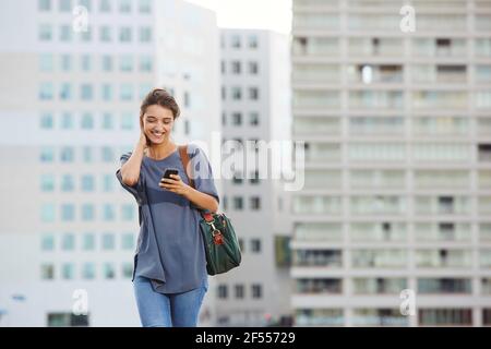 Portrait d'une jeune femme attrayante marchant à l'extérieur et lisant du texte message sur téléphone portable Banque D'Images