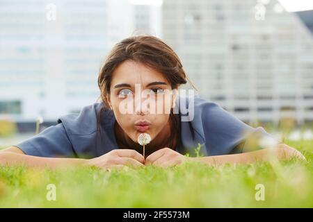 Portrait d'une jeune femme attirante soufflant de pissenlit sur un terrain vert Banque D'Images