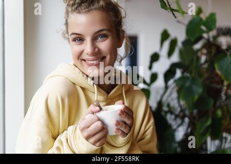 Gros plan sur une belle femme heureuse souriant à l'appareil photo tout en buvant un café. Jolie fille tenant une tasse et regardant l'appareil photo détendu. Une femme qui apprécie Banque D'Images