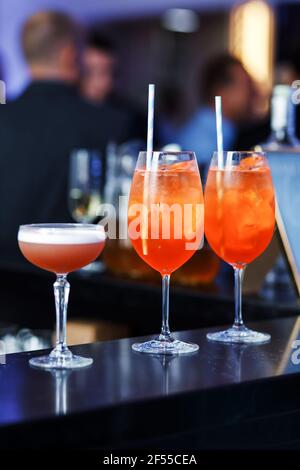 Cinq cocktails colorés préparés par un barman avec des morceaux d'orange et de la glace pilée. Banque D'Images