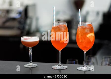 Cinq cocktails colorés préparés par un barman avec des morceaux d'orange et de la glace pilée. Banque D'Images