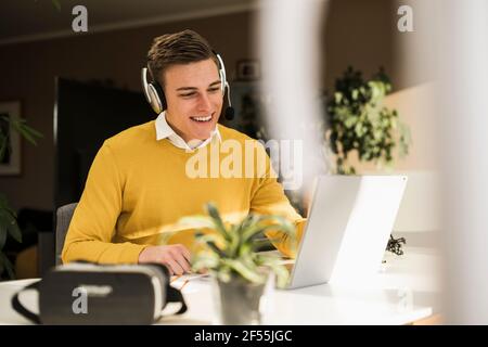 Homme souriant professionnel portant des écouteurs pour assister à une réunion d'affaires à la maison bureau Banque D'Images