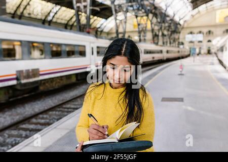 Femme écrivant dans le livre en se tenant sur la plate-forme de chemin de fer Banque D'Images