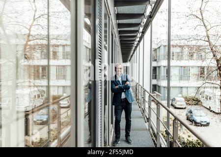 Homme d'affaires avec les bras croisés penché sur la fenêtre de verre dans le bureau balcon Banque D'Images