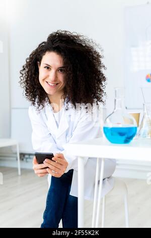 Femme souriante médecin avec téléphone mobile regardant loin dans la clinique Banque D'Images