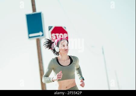 Femme avec un casque regardant loin en courant contre le panneau d'affichage Banque D'Images