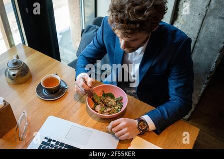 Homme d'affaires ayant une salade tout en étant assis avec un ordinateur portable au café Banque D'Images