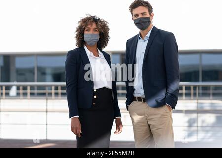 Professionnels avec masque de protection qui se tiennent debout au bureau terrasse du bâtiment Banque D'Images