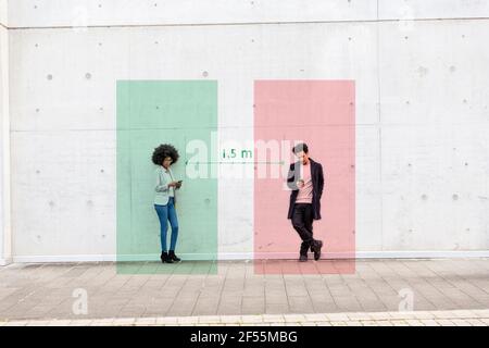 Rectangles visualisant les distances sociales couvrant l'homme et la femme debout à l'extérieur avec les smartphones en main Banque D'Images