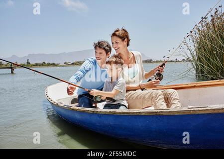 Parents avec canne à pêche assis par son fils en barque lac Banque D'Images