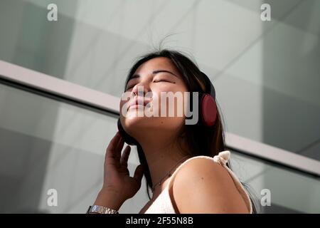 Femme asiatique écoutant de la musique à travers des écouteurs en extérieur Banque D'Images