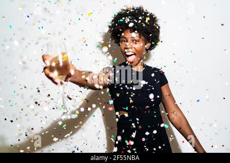 Femme gaie avec flûte à champagne debout au milieu des confettis contre le blanc arrière-plan Banque D'Images