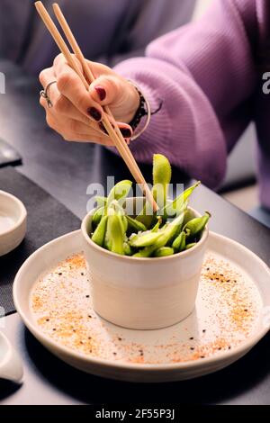 Femme mature mangeant de l'edamame frais avec des baguettes au restaurant Banque D'Images