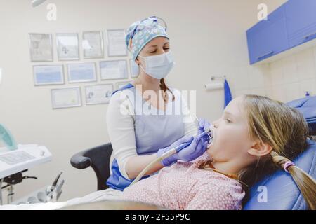 Femme dentiste portant un masque facial de protection examinant petite fille à bureau Banque D'Images