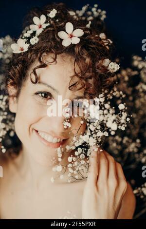 Femme mi-adulte souriante portant des fleurs blanches Banque D'Images