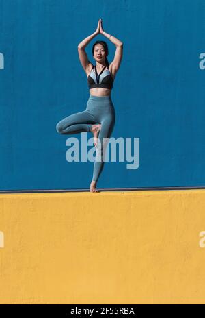 Femme avec les mains classed debout sur une jambe contre le mur Banque D'Images