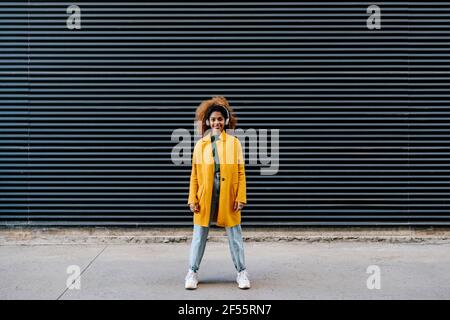 Femme afro souriante avec casque contre le mur Banque D'Images