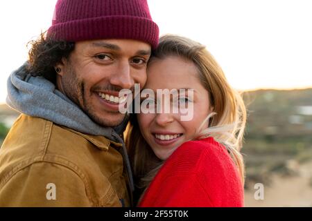 Couple souriant s'embrassant tout en se tenant à l'extérieur pendant le coucher du soleil Banque D'Images