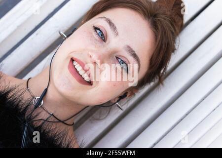 Belle femme souriante écoutant de la musique tout en étant couché sur le banc Banque D'Images