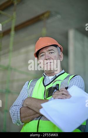 Portrait d'un travailleur de la construction de sexe masculin portant un casque résistant debout avec une croix bras Banque D'Images