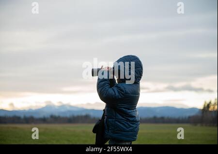 Vue de profil d'un jeune garçon excité debout à l'extérieur dans une belle nature regardant à travers des jumelles. Banque D'Images