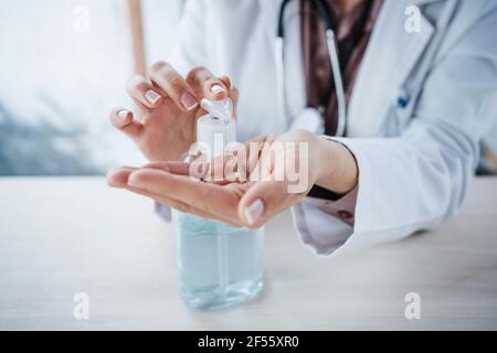 Femme médecin utilisant du gel d'alcool au bureau Banque D'Images