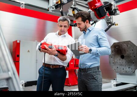 Des ingénieurs masculins travaillant avec des équipements robotisés en usine Banque D'Images