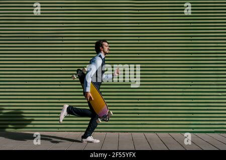 Homme entrepreneur avec longue planche sur la piste de marche par le mur vert Banque D'Images