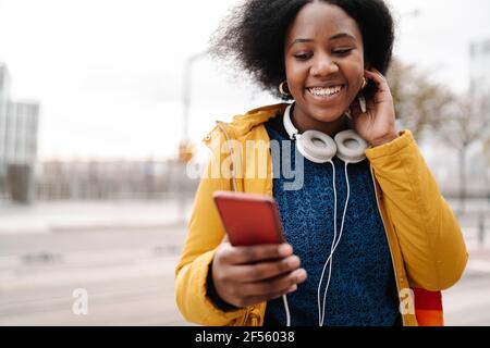 Femme souriante vêtue de vêtements chauds à l'aide d'un téléphone portable Banque D'Images