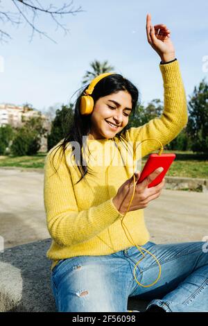 Femme souriante avec un casque dansant tout en tenant le téléphone portable stationnement Banque D'Images