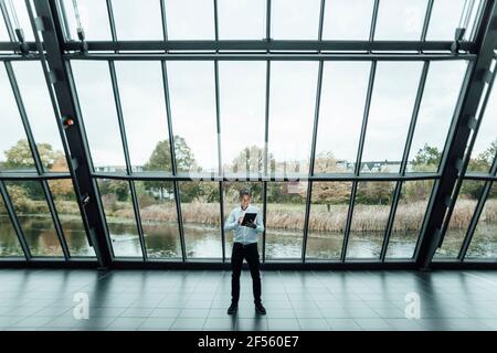Homme d'affaires utilisant une tablette numérique tout en utilisant une tablette numérique contre verre dans le couloir des bureaux Banque D'Images