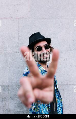 Jeune homme souriant montrant le signe de la paix en se tenant devant de mur Banque D'Images