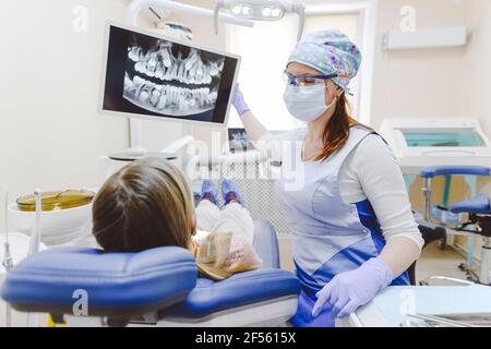 Dentiste de sexe féminin montrant des rayons X à une petite fille qui se trouve dans des dentistes chaise Banque D'Images