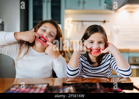 Des filles enjouées avec maquillage sur le visage taquant tout en étant assis table à manger dans la cuisine Banque D'Images