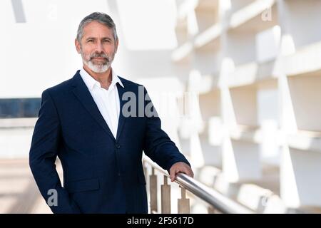 Homme d'affaires mature regardant en se tenant debout près de la rampe sur la terrasse du bureau Banque D'Images