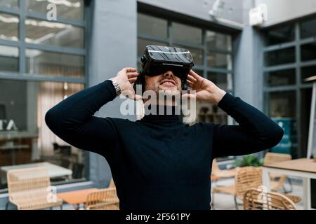 Homme d'affaires souriant utilisant un casque de réalité virtuelle lorsqu'il est assis dans un café Banque D'Images