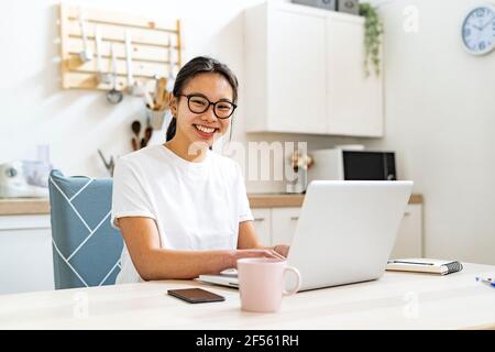 Femme souriante assise près d'une table avec un ordinateur portable à la maison Banque D'Images
