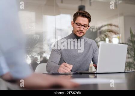 Homme entrepreneur écrivant sur le presse-papiers par ordinateur portable au bureau Banque D'Images