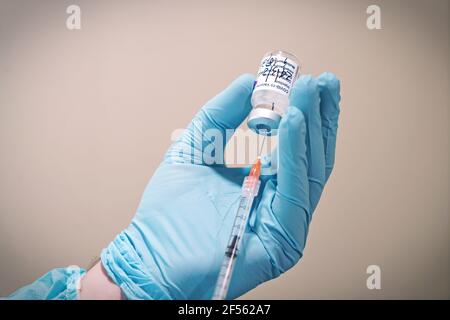Flacon de vaccin COVID-19 produit par AstraZeneca. La main du médecin dans un gant médical tient une bouteille avec un vaccin coronavirus. Mise au point sélective. Turin, Banque D'Images