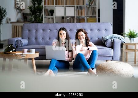 Fille souriante avec ordinateur portable, assis par une mère tenant un journal pendant assis sur le sol à la maison Banque D'Images