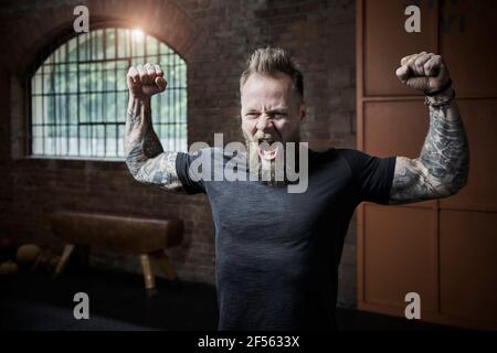 Un athlète masculin crie tout en fléchissant ses muscles en salle de sport Banque D'Images