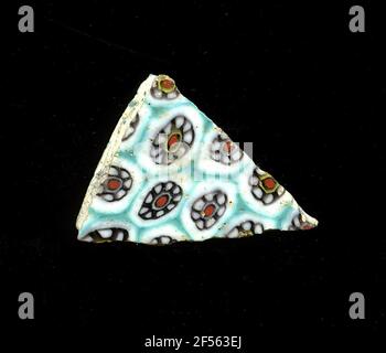 Fragment de mosaïque de verre. Le petit fragment de verre montre plusieurs fleurs dans la technologie millefiori sur fond blanc, qui sont séparées l'une de l'autre par une grille turquoise sous la forme d'un nid d'abeille. Une fleur se compose d'un point rouge avec un contour noir comme noyau. Trois des fleurs sont un cercle blanc avec une partie des fleurs, et d'autres un jaune. Les cercles blancs avec contour noir forment les pétales autour de ce noyau. À l'époque romaine, il utilisait du verre coloré et ornementé pour les navires, les mosaïques, les décorations murales et les ornements de meubles. Pour la production, des lunettes de différentes couleurs ont été moulées Banque D'Images