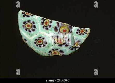 Fragment d'un vaisseau. Une faible courbure du fragment de verre et une plicature permettent l'affectation à un vaisseau, probablement une coque. Le shard turquoise recouvre une grille blanche qui ressemble à des nids de miel. Il y a des fleurs dans la technologie Millefiori. À un point rouge avec des bordures turquoise, jaune et violet est un ruban blanc, dans lequel les petits points violets sont disposés comme des pétales. Pour la production, des verres de différentes couleurs ont été moulés dans des tubes et des tiges. Elles étaient comprimées et chauffées, ce qui entraînait une longue barre. Le verre coupé en tranches de ​​now avait des motifs amorphes ou floraux différents. Par la suite, plusieurs de ces plaquettes Banque D'Images