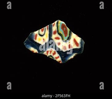 Fragment de mosaïque de verre. Le fragment irrégulièrement brisé a des fleurs de millefiori sur fond bleu; il s'agit de points rouges avec bordure blanche pour cercle disposés avec des cercles bleu, jaune, turquoise et rouge de l'extérieur; un autre type de fleurs avec des points jaunes et rouges alternés avec bordure blanche avec des cercles bleus, blancs et rouges à l'intérieur. À l'époque romaine, on utilisait du verre coloré et ornementé pour les navires, les mosaïques, les décorations murales et les ornements de meubles. Pour la production de verres de différentes couleurs à tubes et barres façonnées. Elles étaient comprimées et chauffées, ce qui entraînait une longue barre. Le verre tranché Banque D'Images