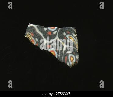 Fragment de mosaïque de verre. Le petit fragment de verre montre sur fond rouge foncé ou violet une grille de lignes blanches rappelant les nids d'abeilles. Dans les champs, les fleurs sont vues dans la technologie millefiori. Ils se composent d'un point jaune avec un contour rouge et blanc pour modifier alternativement les points rouges et blancs circulaires. À l'époque romaine, ils utilisaient du verre coloré et ornementé pour les navires, les mosaïques, les décorations murales et les ornements de meubles. Pour la production de verres de différentes couleurs à des tubes et tiges en forme. Elles étaient comprimées et chauffées, ce qui entraînait une longue barre. Le verre coupé en tranches de ​​now avait un amorphoo différent Banque D'Images