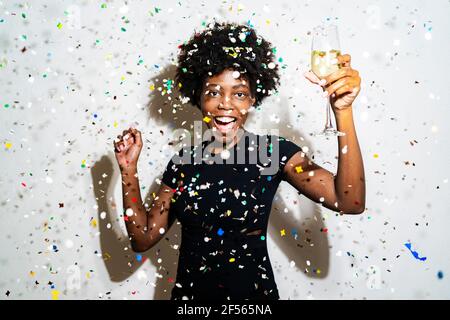 Une femme heureuse avec une flûte à champagne dansant au milieu de confetti sur fond blanc Banque D'Images