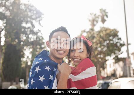 Couple souriant tout en se tenant enveloppé dans le drapeau américain dehors Banque D'Images