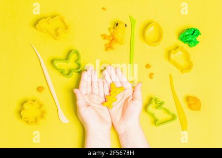 Les enfants jouent avec de l'argile à modeler colorée sur fond jaune. Jeu éducatif avec argile. Enfants sculptant des figures d'argile. Devel Banque D'Images